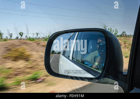 View through rear-view mirror of a car moving on highway through desert in high speed with surrounding motion blurred copy space Stock Photo