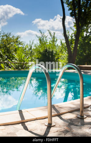 Pool ladder close up on swimming pool in green garden, vertical Stock Photo