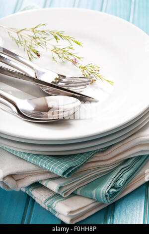 A stack of clean white plates with silverware on blue napkins Stock Photo