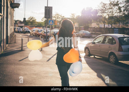 Young beautiful reddish brown hair caucasian woman viewed from back walking through the street playing with baloon in shape of heart - carefreeness, childhood, youth concept Stock Photo