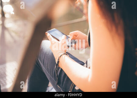 Close up of the hands of a woman reddish brown air using a smartphone seated on a staircase - technology, social network, communication concept - dressed with black shirt and blue jeans Stock Photo
