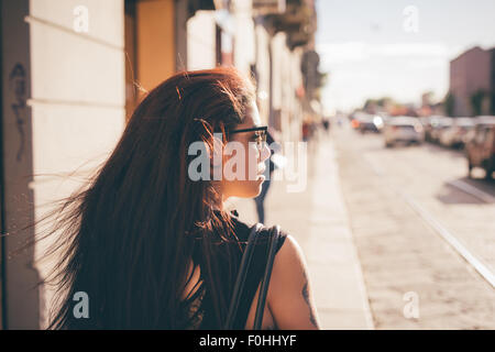 Half length of a young reddish brown hair caucasian woman viewed from back - youth, freshness, carefreeness concept - dressed with blue jeans ans black shirt - backlight Stock Photo