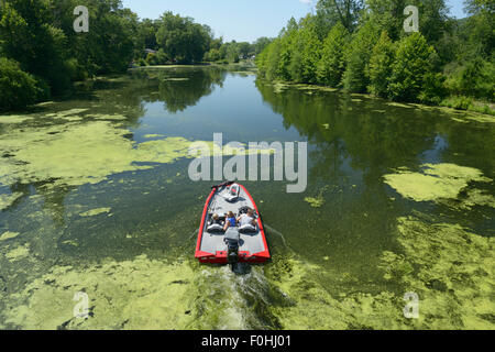 People in boat moving through polluted water undergoing eutrophication and an algae bloom, Ramapo River, NJ Stock Photo