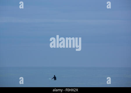 Blue flat horizon with one surfer waiting with a surfing board the perfect wave early in the morning, Mancora. Peru Stock Photo