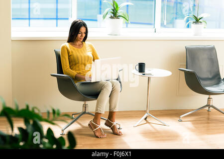 Beautiful casual businesswoman sitting on office chair and using laptop in office Stock Photo