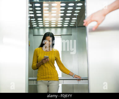 Portait of a happy businesswoman using smartphone in elevator Stock Photo