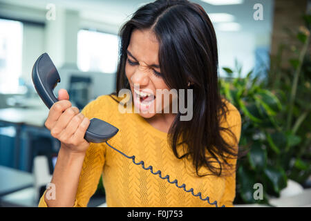 Angry businesswoman shouting on phone in office Stock Photo
