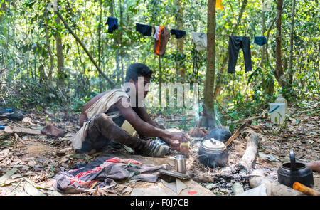 Young man of the Orang Asil tribe sitting on the floor in the jungle and making tea, native, indigenous people Stock Photo