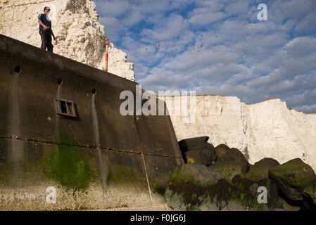 Man standing on sea wall, Saltdean, Sussex, low angle, cliffs in background Stock Photo