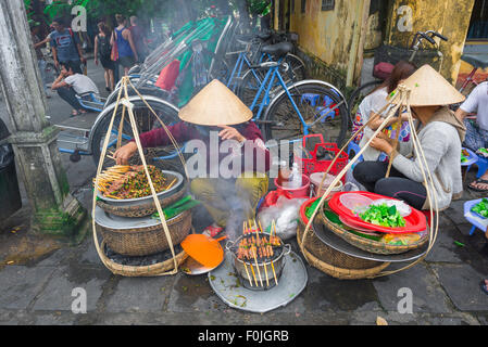Vietnam street food, two women grill pork kebabs in the street near the waterfront in Hoi An, Central Vietnam.