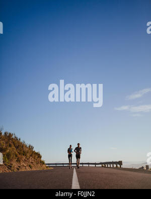 Distant shot of two young runners running on open country road with blue sky. Two young man and woman jogging outdoors on a summ Stock Photo