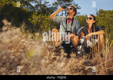 Outdoor shot of young couple sitting together taking a break on hike. Caucasian man and woman drinking water while out hiking. Stock Photo