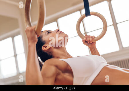 Close up shot of strong young woman doing pull-ups with gymnastic rings. Fitness female athlete exercising at gym. Stock Photo