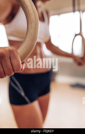 Close up shot of female athlete holding gymnastic rings. Focus on woman hands exercising with rings at gym. Stock Photo