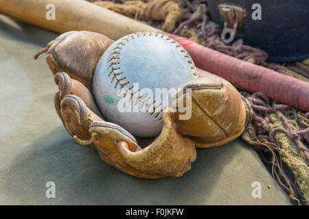 Old worn leather baseball glove with bat in the background Stock Photo
