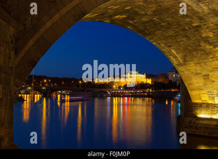 View at night across the Vltava River in Prague under the arches of Charles Bridge