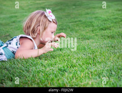 Little beautiful girl  lies on the green grass outdoors in summer garden. Stock Photo