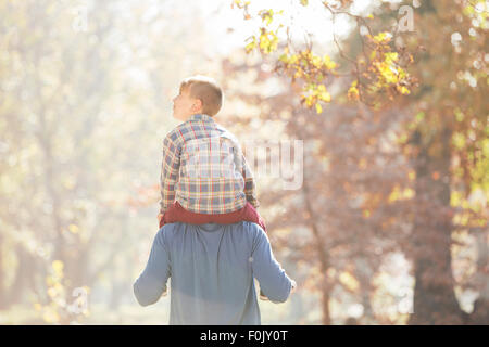 Father carrying son on shoulders below autumn leaves Stock Photo