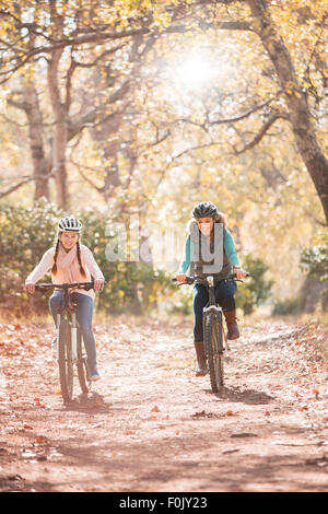 Mother and daughter bike riding on path in woods Stock Photo