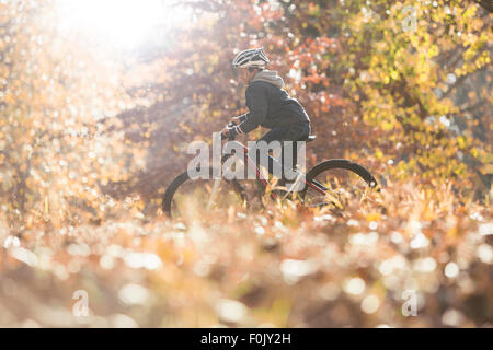Boy bike riding in woods with autumn leaves Stock Photo