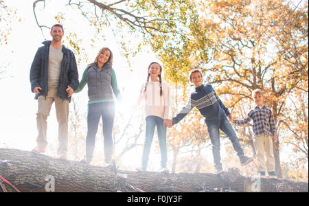 Portrait smiling family holding hands on fallen log in a row Stock Photo