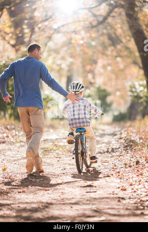 Father teaching son to ride bicycle on path in woods Stock Photo