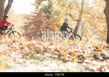 Boy and girl bike riding in woods with autumn leaves Stock Photo