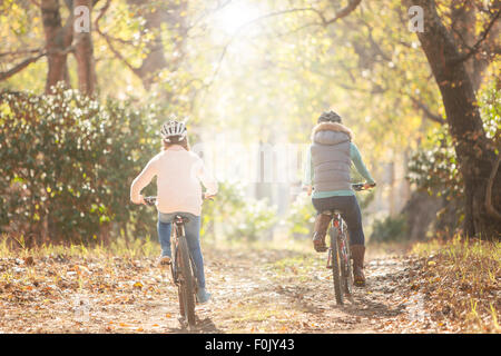 Mother and daughter bike riding on path in woods Stock Photo