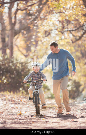 Father teaching son to ride a bicycle on path in woods Stock Photo