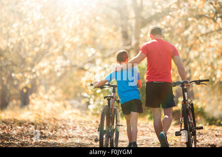 Affectionate father and son walking mountain bikes on path in woods Stock Photo