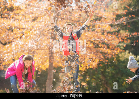 Playful boys and girl running and jumping in autumn leaves Stock Photo