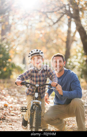 Portrait smiling father teaching son to ride a bike in woods Stock Photo