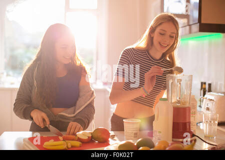 Teenage girls making smoothie in sunny kitchen Stock Photo