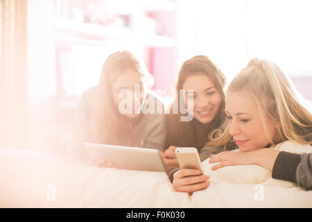 Teenage girls using cell phone and digital tablet in sunny bedroom Stock Photo