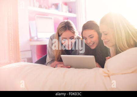 Teenage girls using digital tablet on bed in sunny bedroom Stock Photo