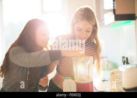 Teenage girls making smoothie in sunny kitchen Stock Photo