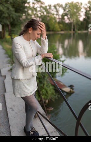 Young woman looking sadly on a harbor with forehead supported on her hand Stock Photo