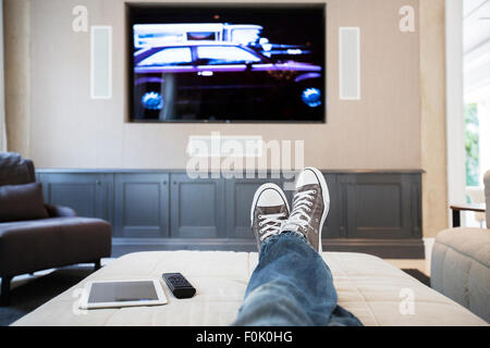 Woman’s feet on ottoman watching TV Stock Photo