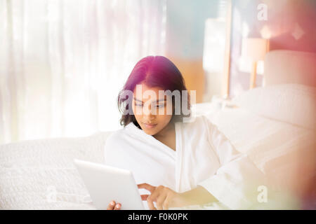Woman in bathrobe using digital tablet on bed Stock Photo