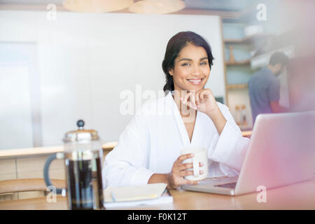 Portrait smiling woman in bathrobe drinking coffee at laptop Stock Photo