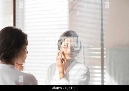 Woman applying moisturizer to cheek in bathroom mirror Stock Photo