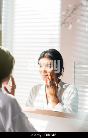 Woman applying moisturizer to face in bathroom mirror Stock Photo