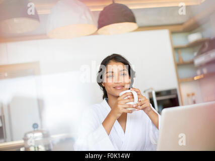 Portrait confident woman in bathrobe drinking coffee at laptop Stock Photo