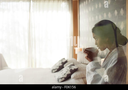 Woman in bathrobe sipping coffee in bedroom Stock Photo