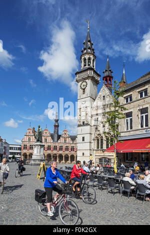 Belfry and elderly tourists cycling past outdoor café on the town square in Aalst / Alost, East Flanders, Belgium Stock Photo