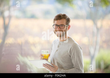 Portrait smiling man drinking orange juice and using digital tablet on patio Stock Photo