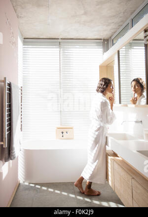 Woman in bathrobe examining face in bathroom mirror Stock Photo