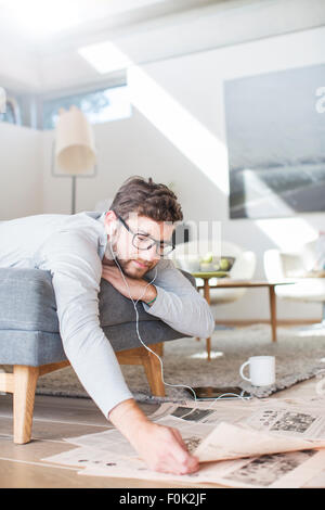 Man with headphones reading newspaper and drinking coffee in living room Stock Photo