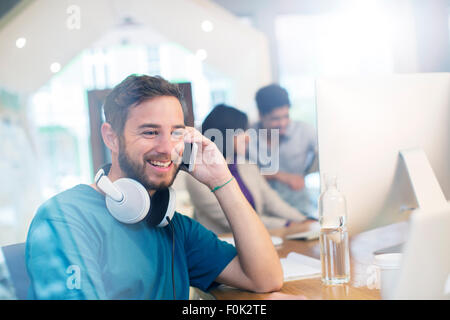 Smiling creative businessman with headphones talking on cell phone in office Stock Photo