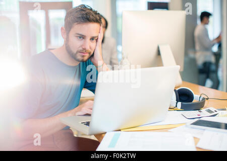 Serious creative businessman using laptop with head in hands in office Stock Photo